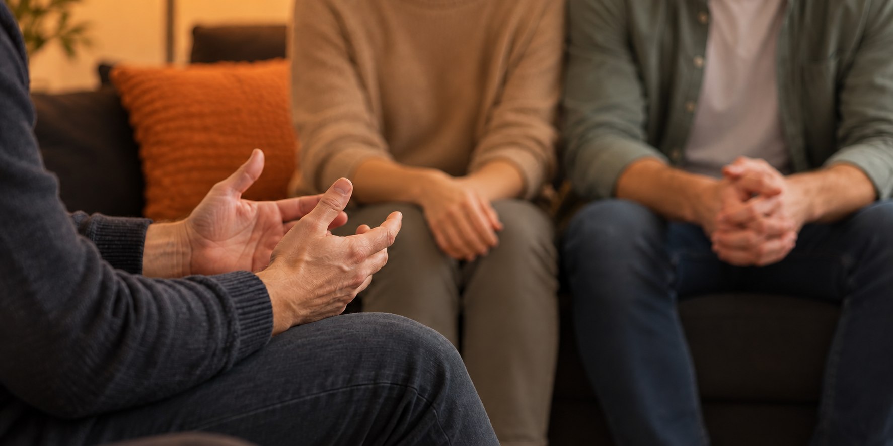 Symbolbild: Ein Paar sitzt in einem Coaching-Gespräch; im Vordergrund gestikulieren die Hände des Beraters.